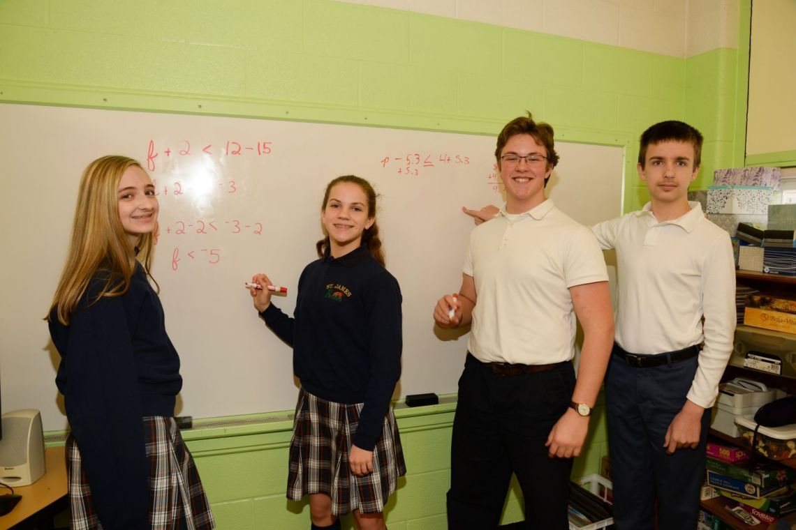 A group of students are standing in front of a white board with math equations on it
