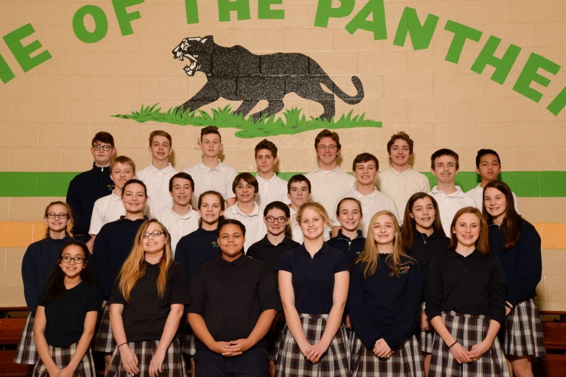 A group of students pose for a picture in front of a panther logo