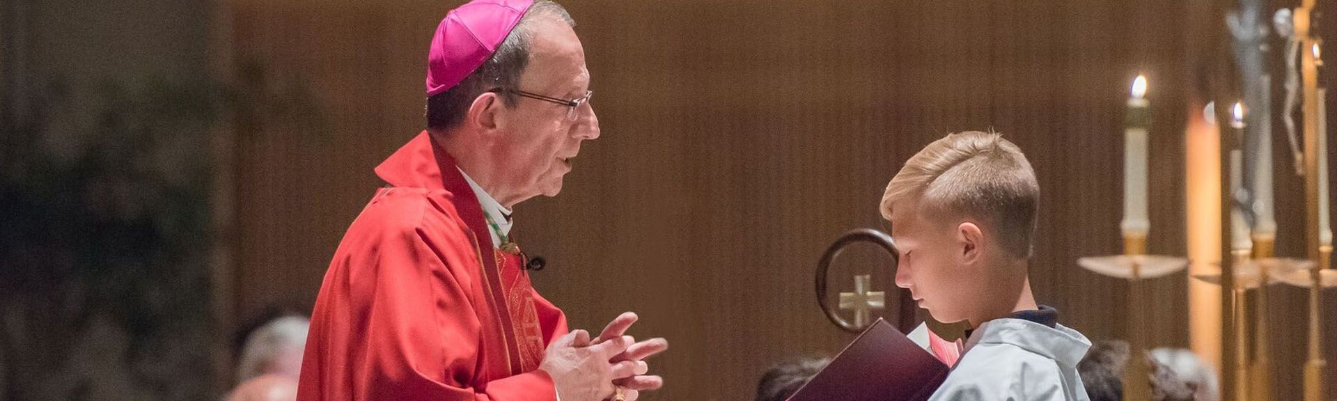A man in a red robe is talking to a young boy in a church.