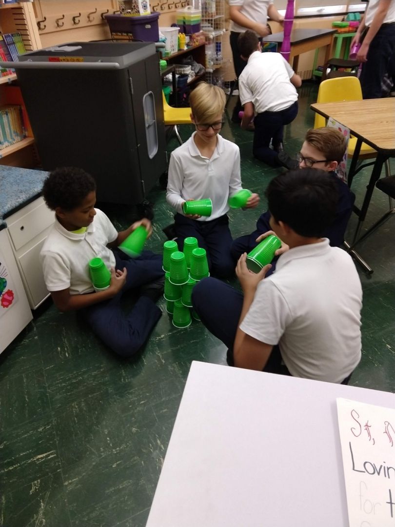 A group of children are sitting on the floor playing with green cups