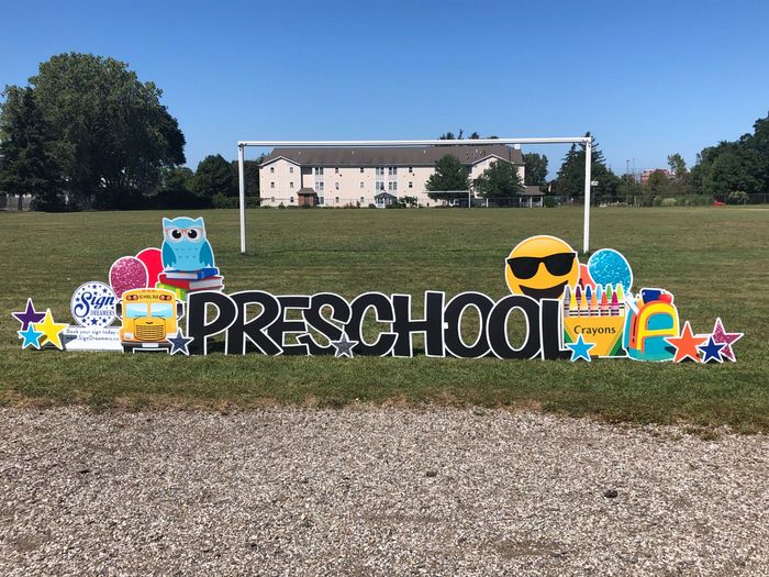 A sign that says preschool is in a grassy field