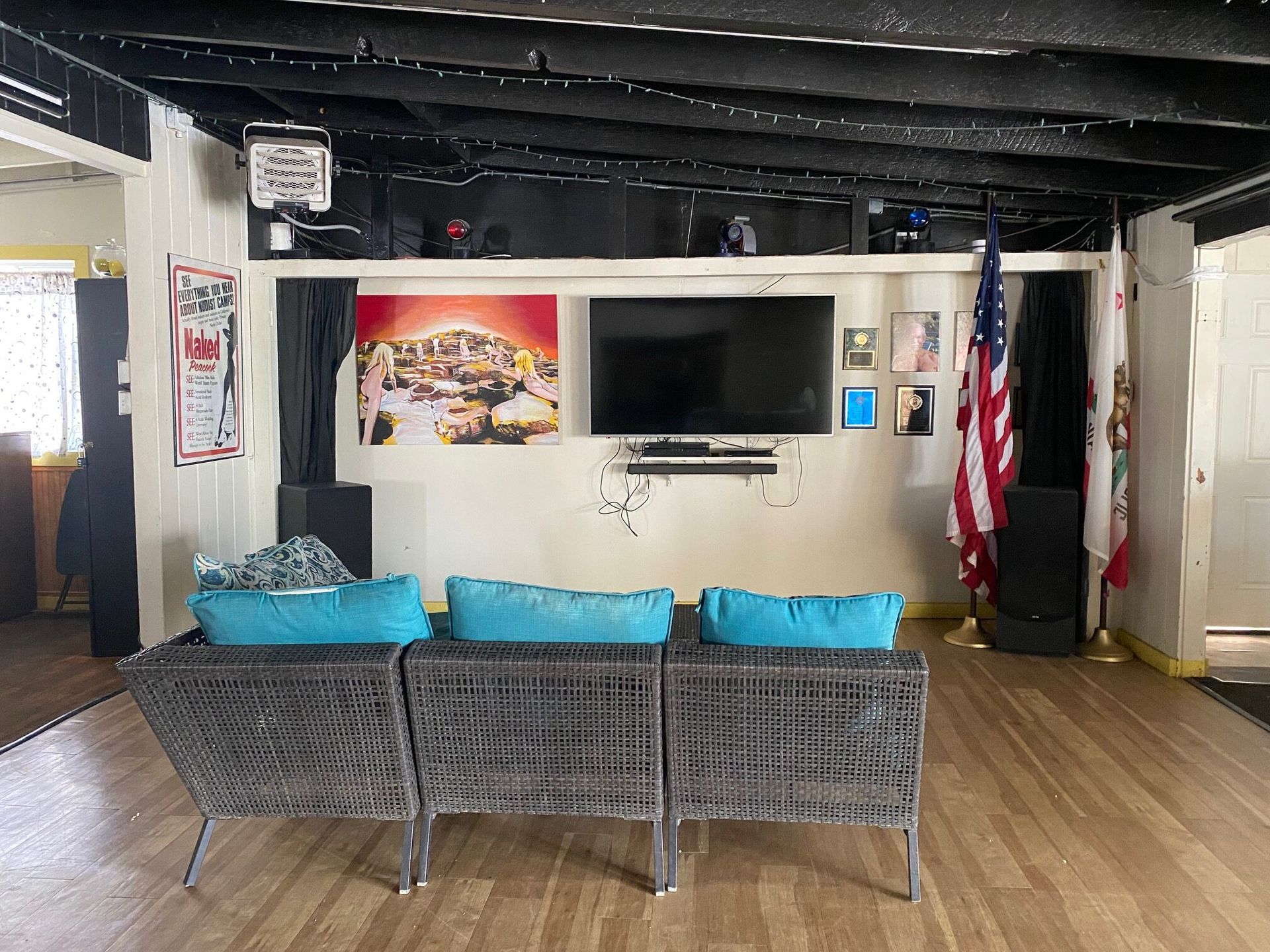 A room with a grey wicker sofa, blue cushions, a wall-mounted TV, artwork, and an American flag on a stand.