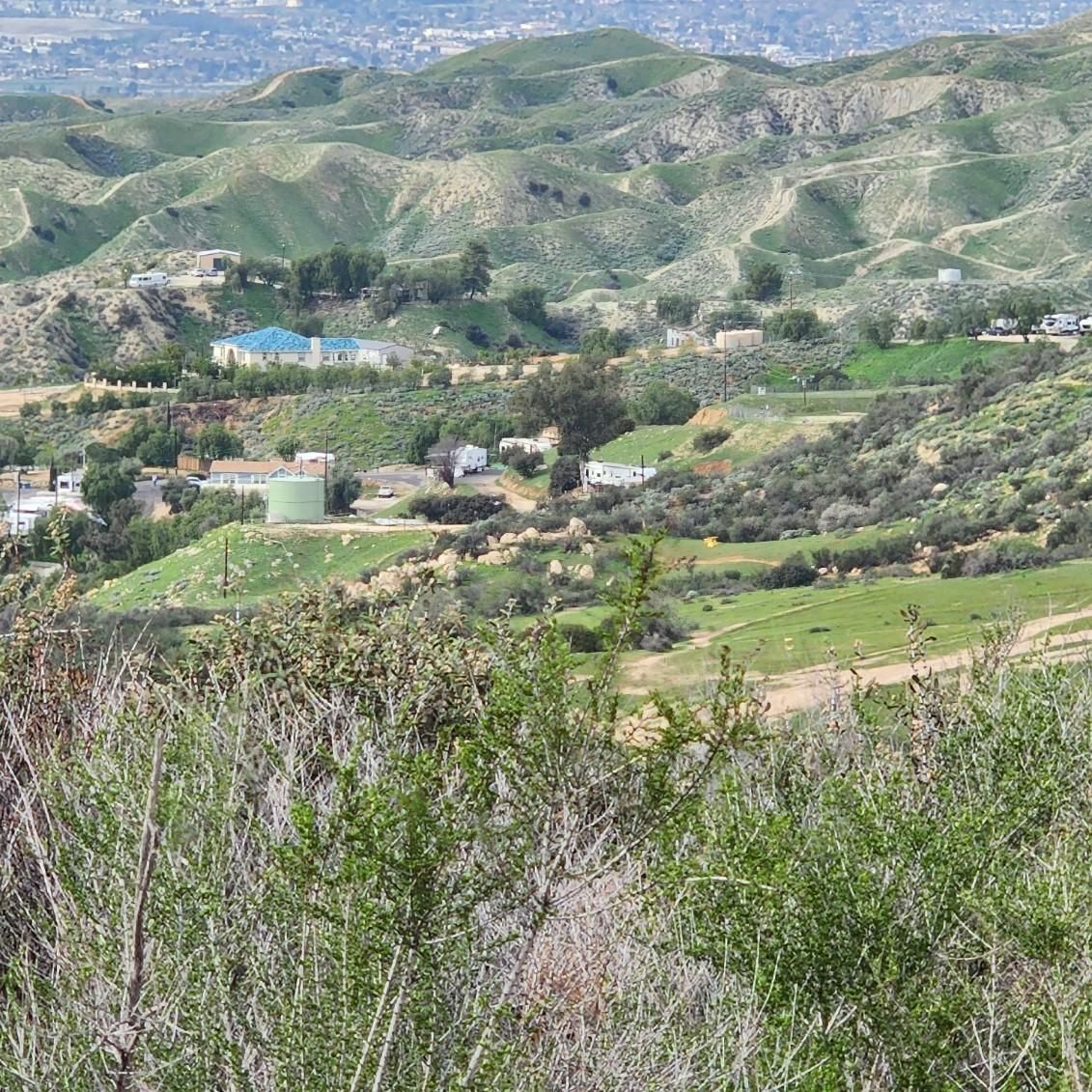 A rolling, green, hilly landscape with scattered houses, trees, and a distant town under a clear, bright sky.