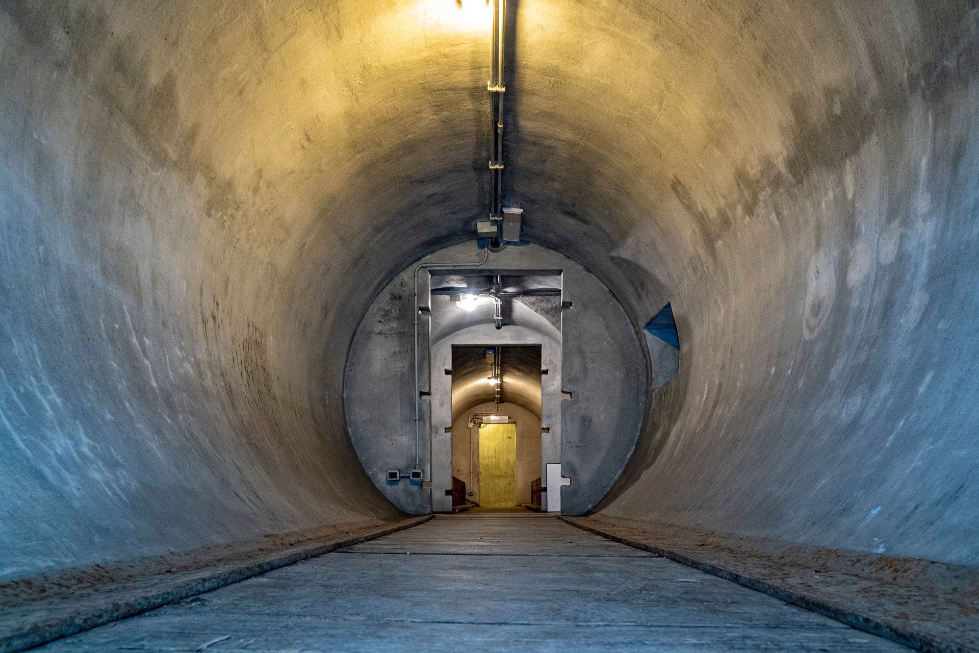 Concrete tunnel interior with yellow-lit doorway at the end.