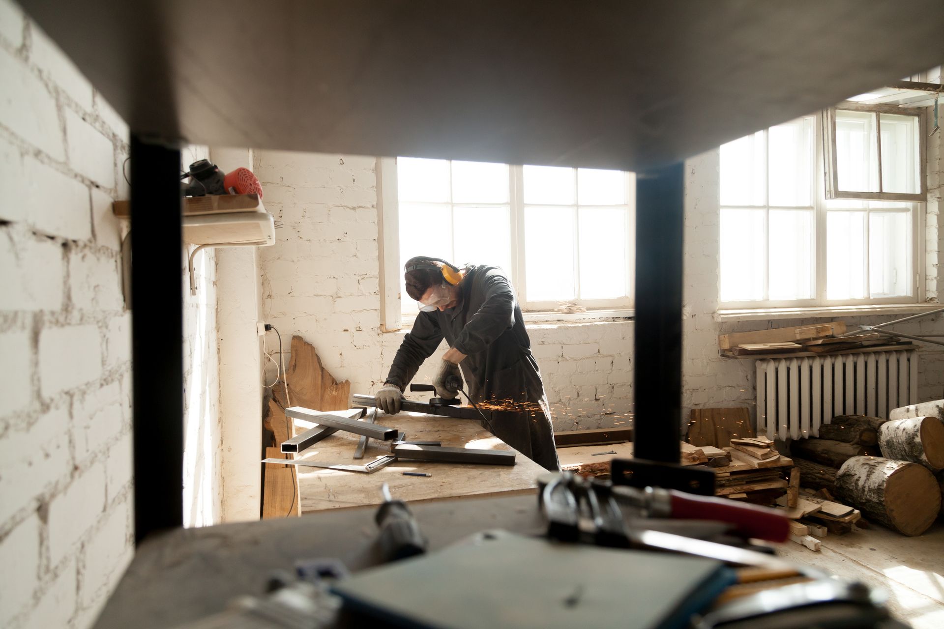 A worker in overalls sands wood in a bright workshop. Brick walls, tools scattered.