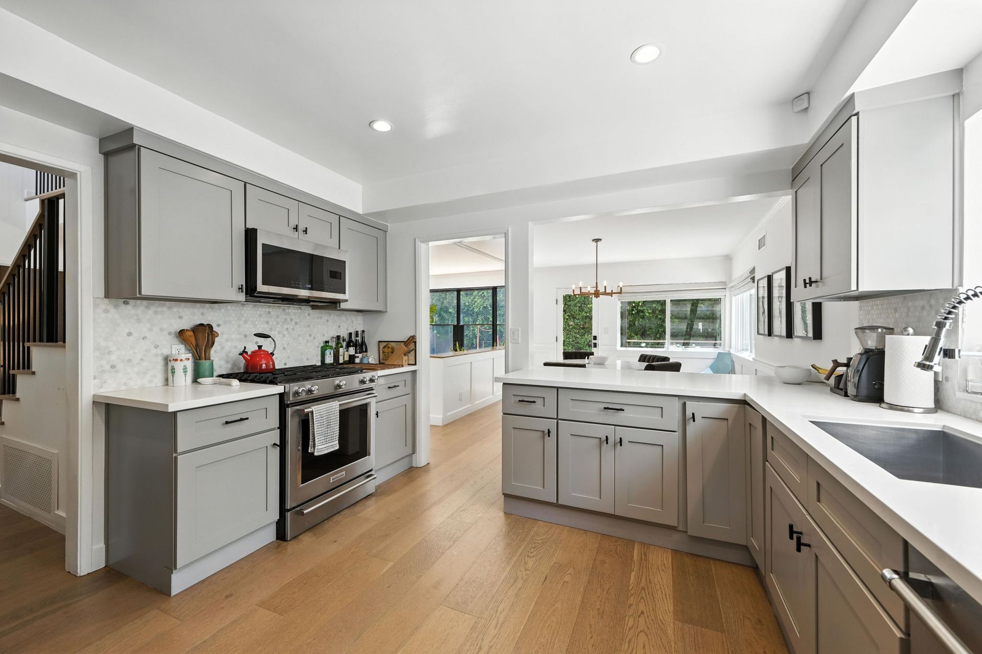 Modern kitchen with gray cabinets, white countertops, stainless steel appliances, and light wood flooring.