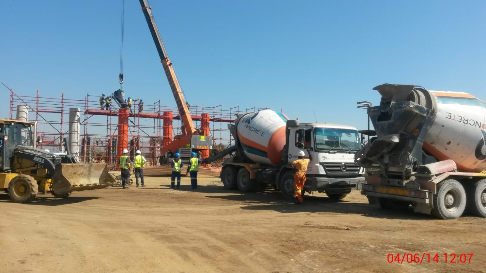 Construction site with workers, crane, cement trucks, and a bulldozer on a sunny day.