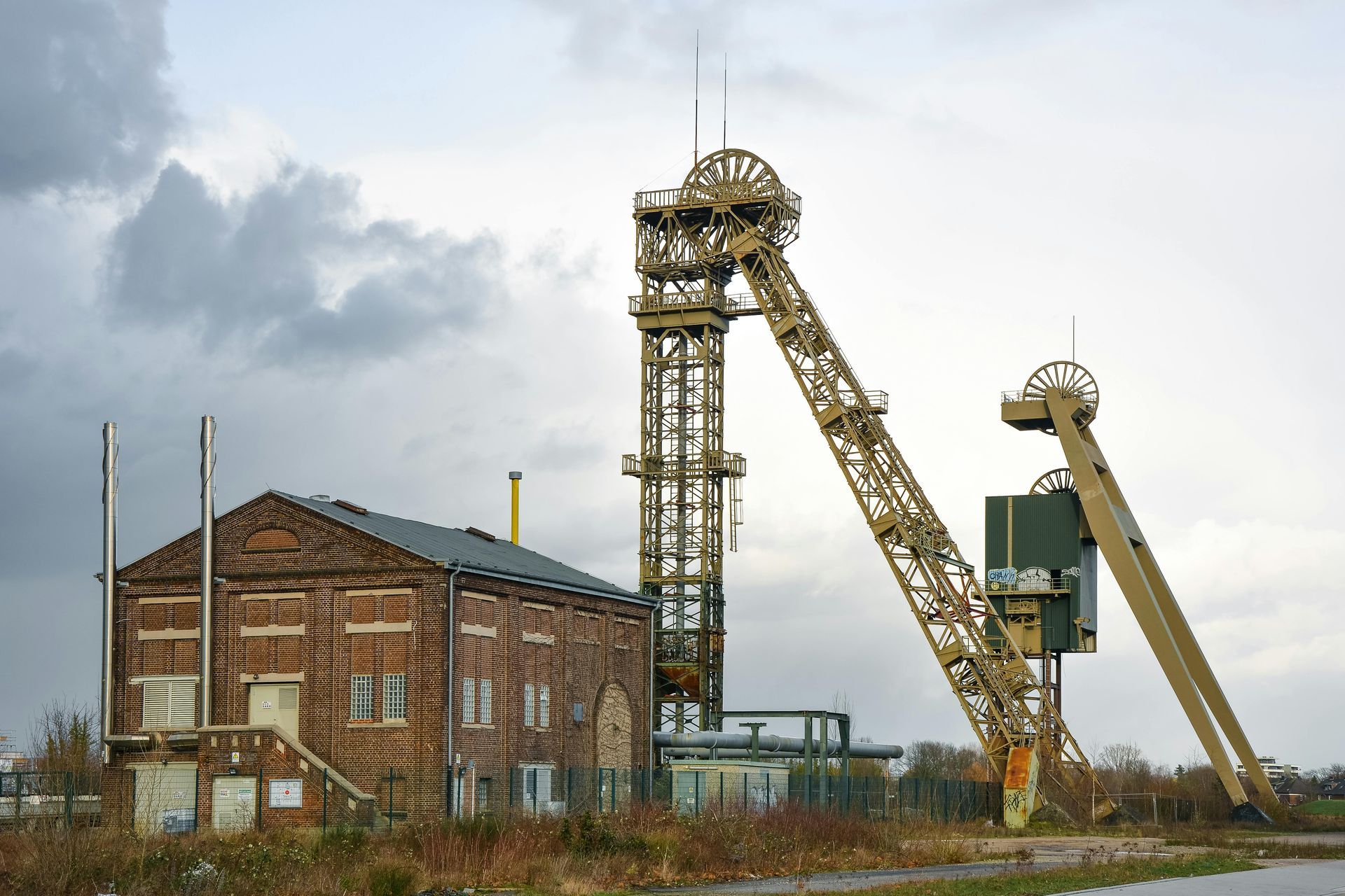 A brick building and two tall, yellow mine structures under a cloudy sky.