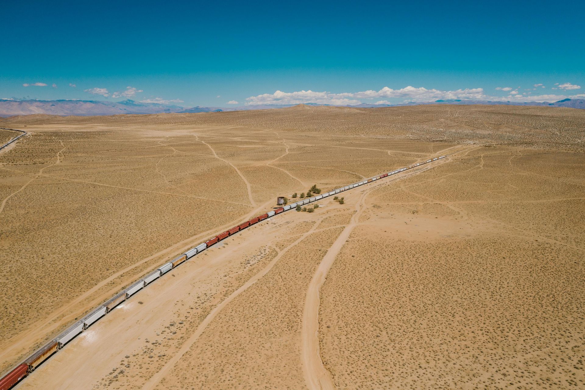 A long train traveling through a vast, arid desert landscape under a clear, blue sky.