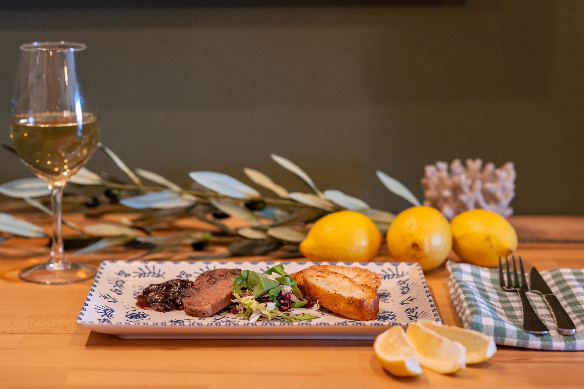 Plato de comida con copa de vino, limones y cubiertos sobre una mesa de madera.