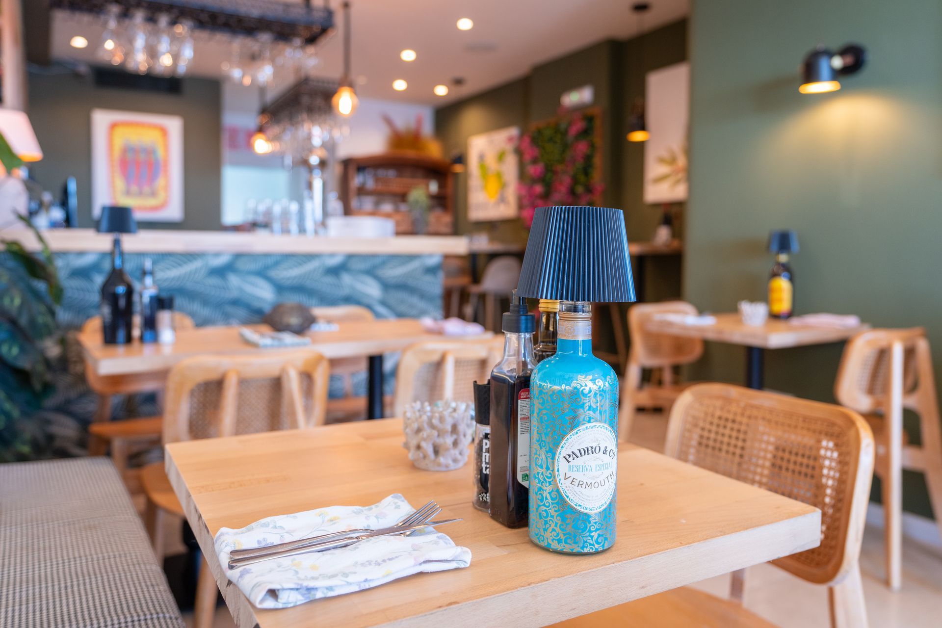 Interior de restaurante con mesas dispuestas para cenar, paredes verdes y bar al fondo.