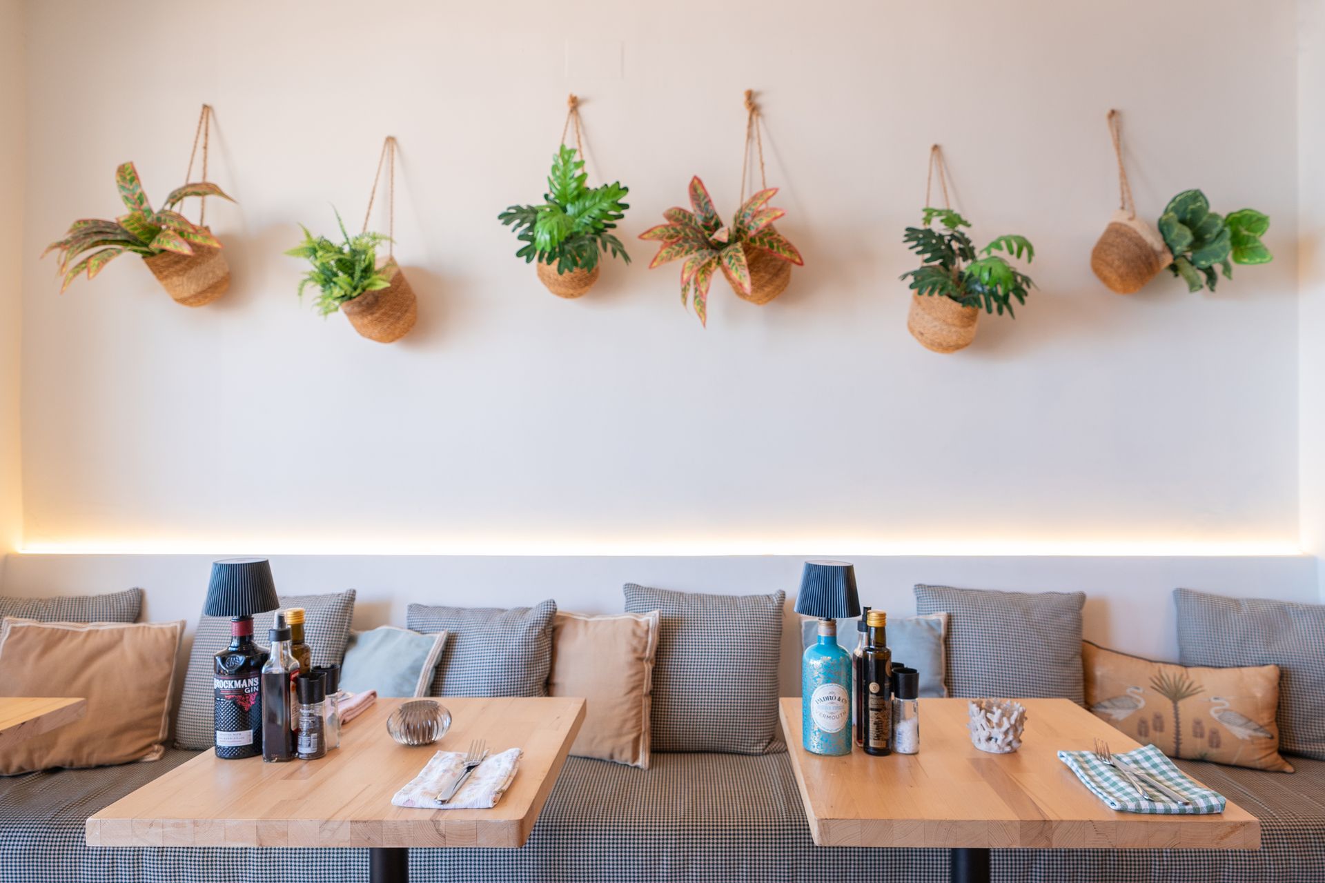 Interior del restaurante: pared con plantas colgantes sobre un banco acolchado, mesas de madera.