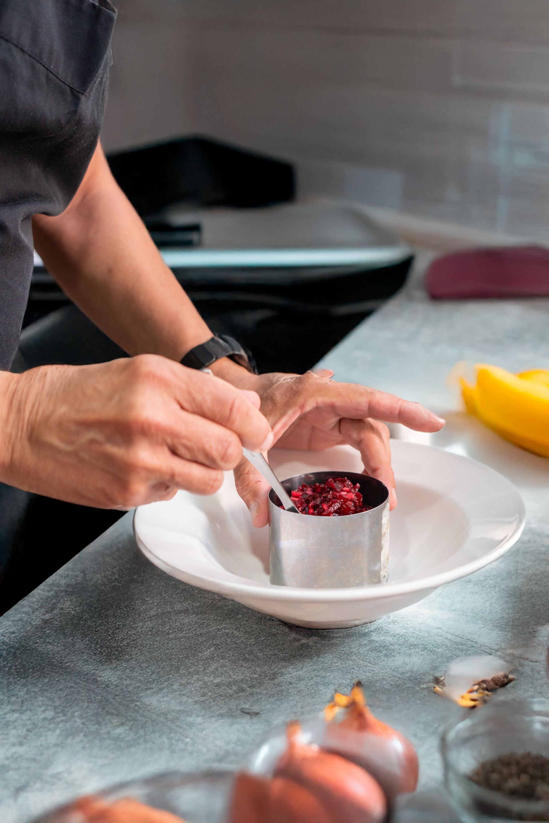 Persona que utiliza un molde de anillo para emplatar un plato con un ingrediente rojo en su interior, sobre un plato blanco.