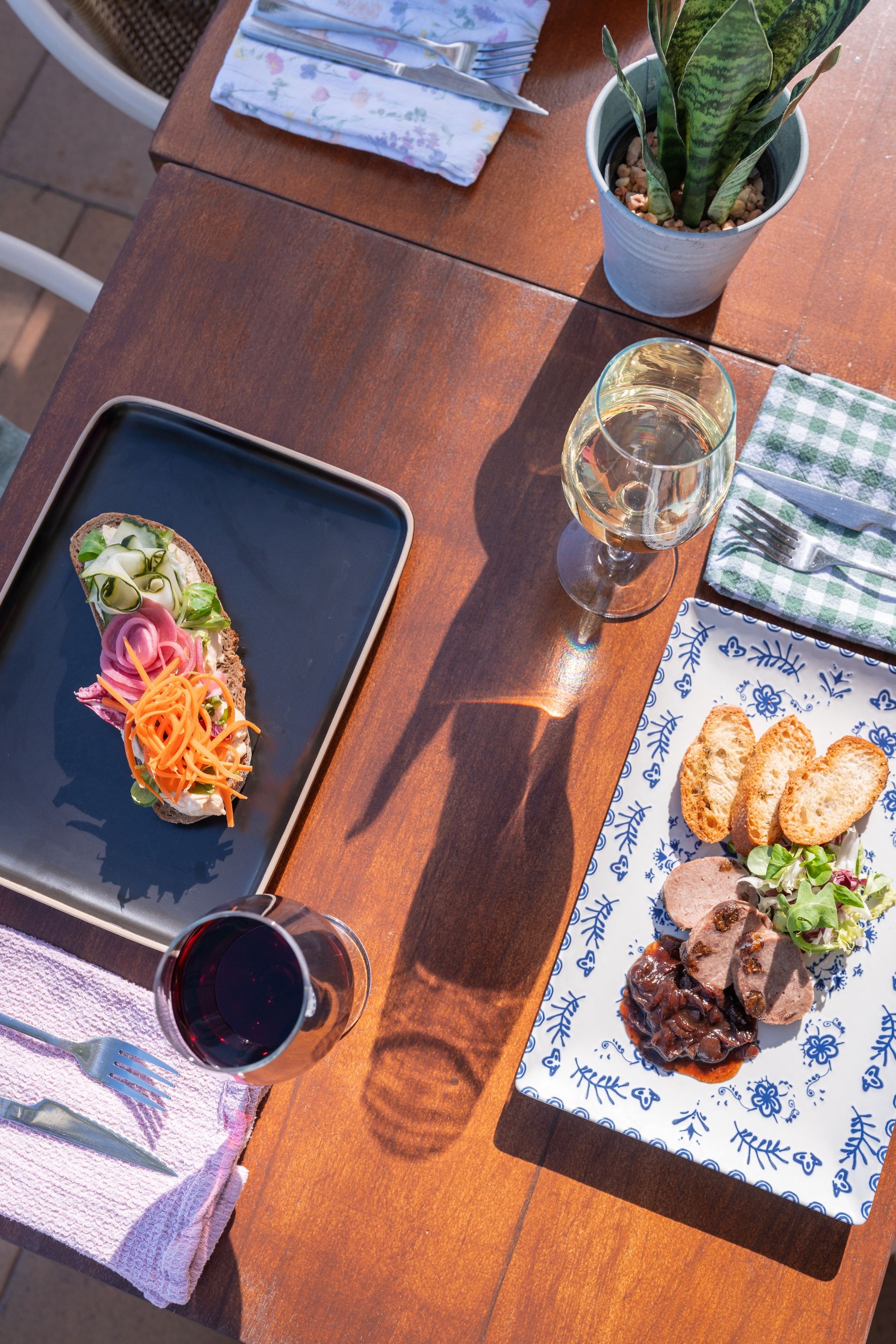 Vista aérea de una mesa de comedor con comida, bebidas, servilletas y una planta.