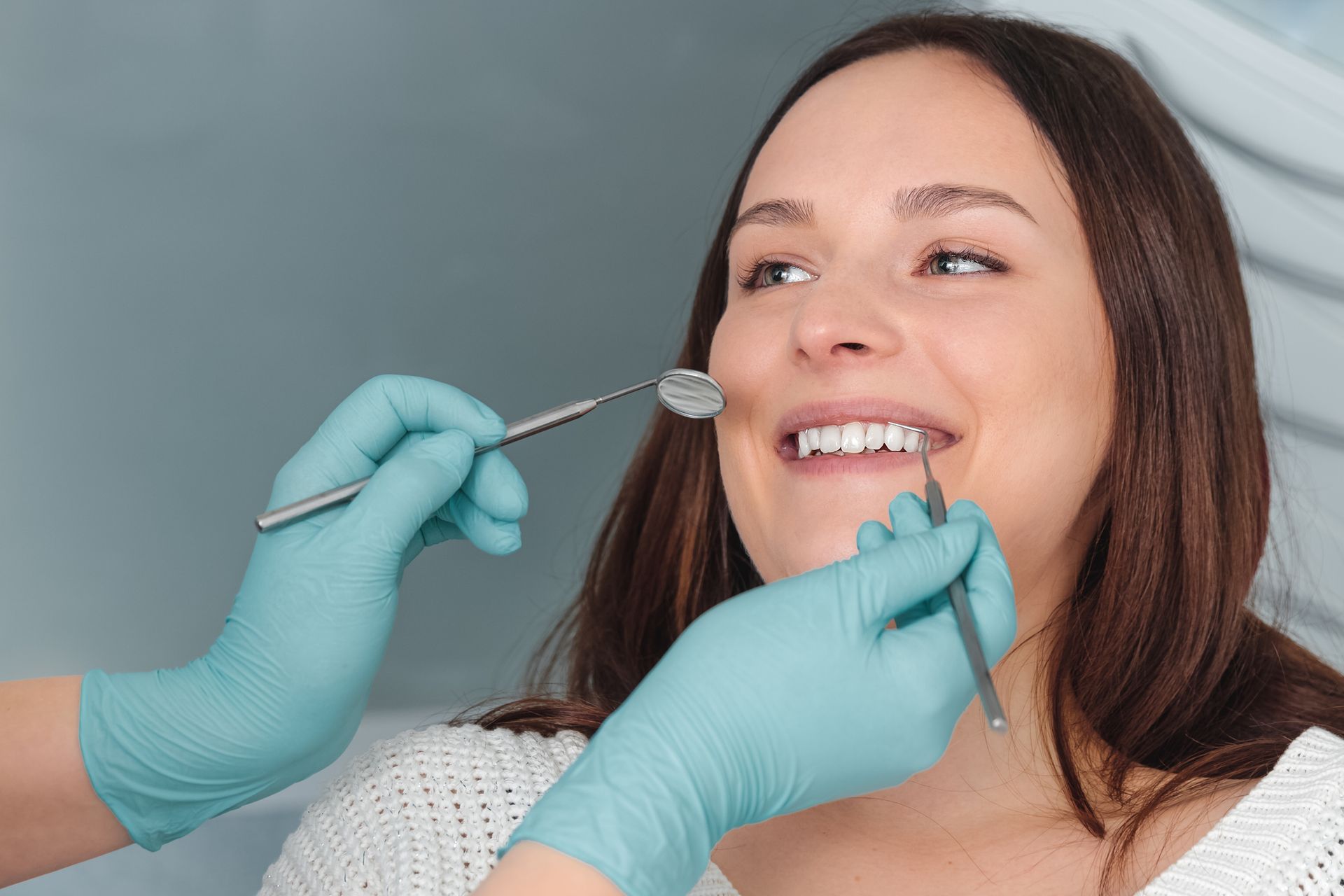 Smiling woman in dental chair, dentist in blue gloves holding mirror and scaler.