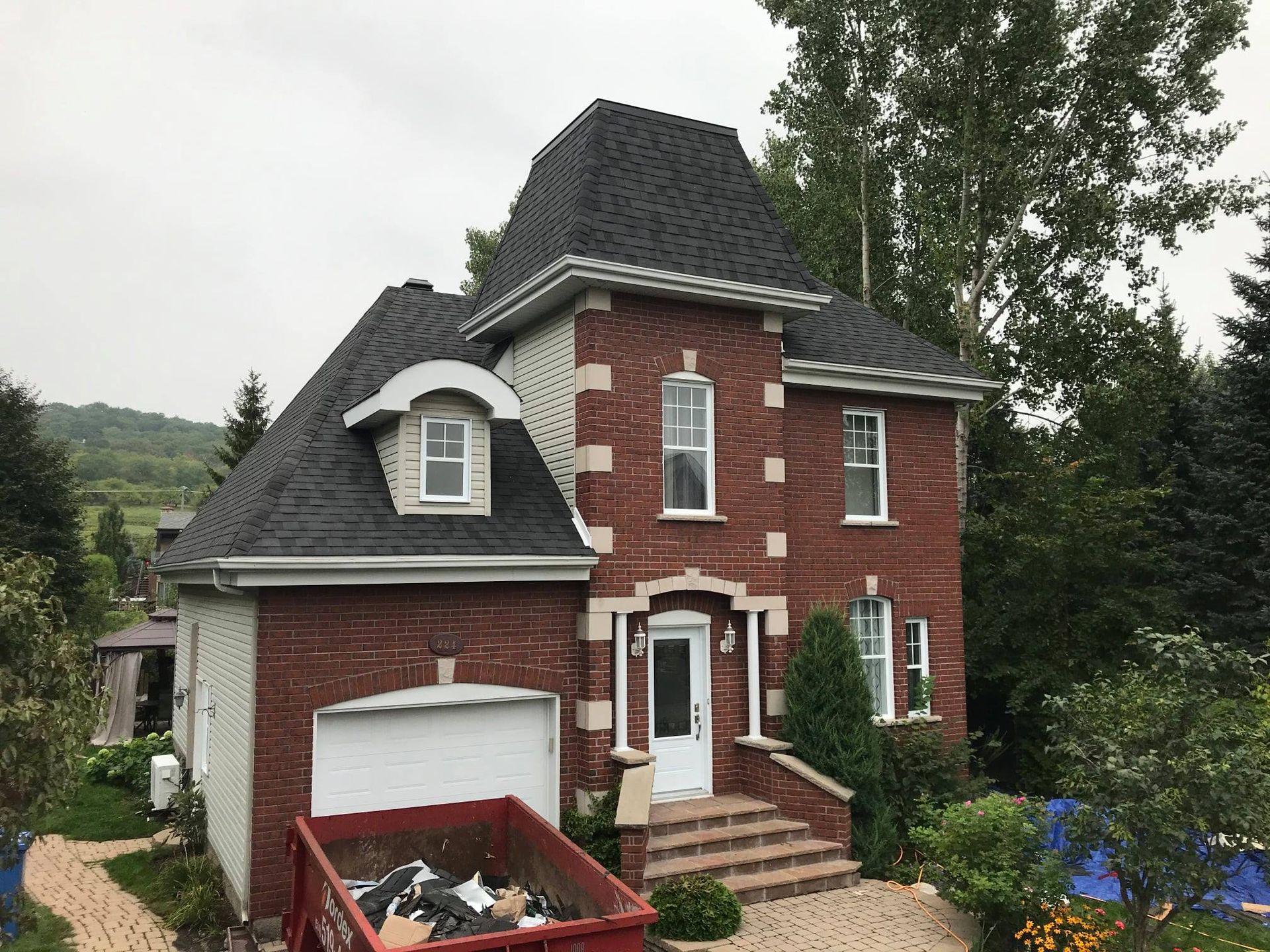 Une grande maison en briques avec une benne à ordures devant.