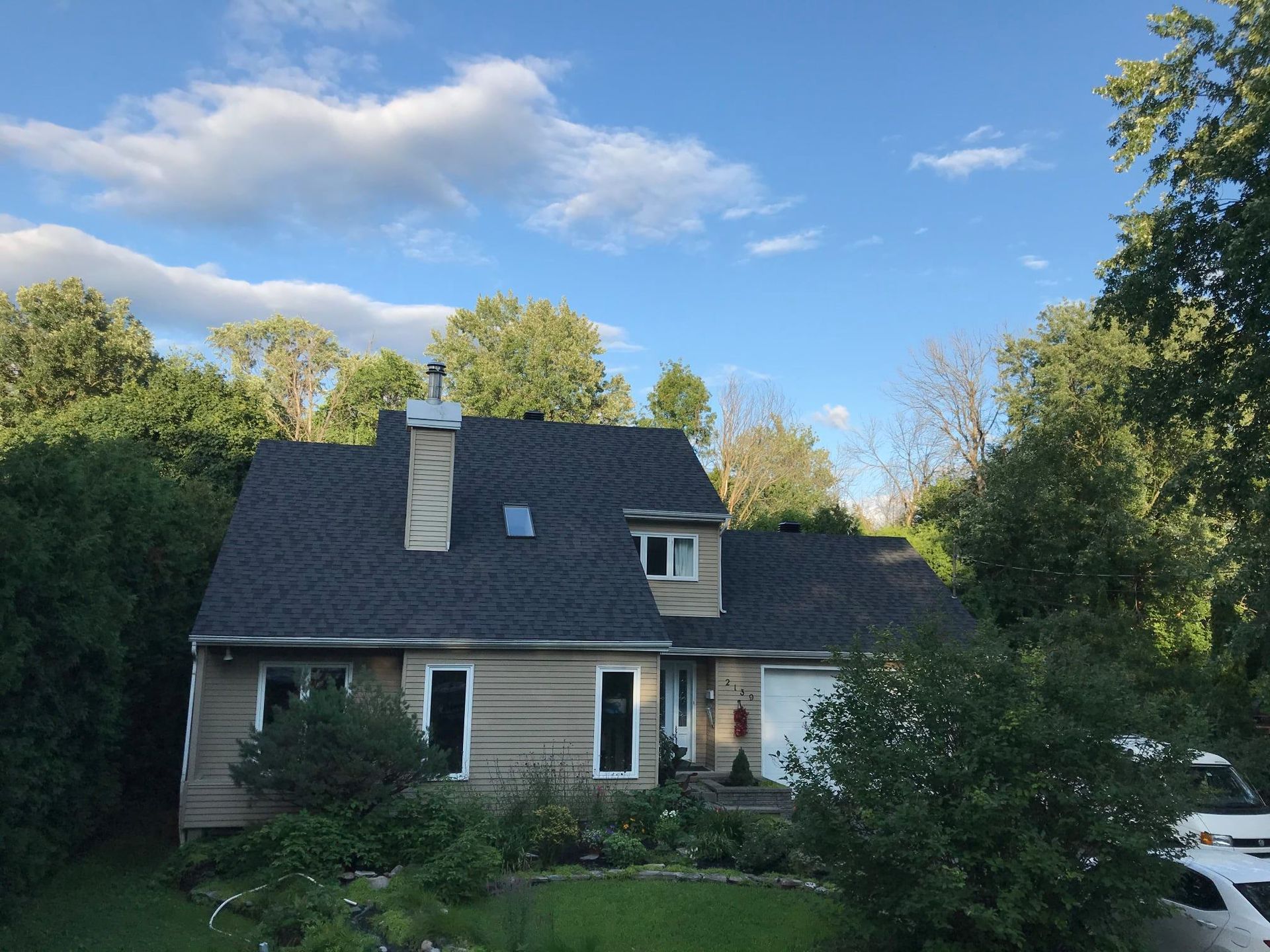 Une maison au toit noir est entourée d'arbres et de buissons.