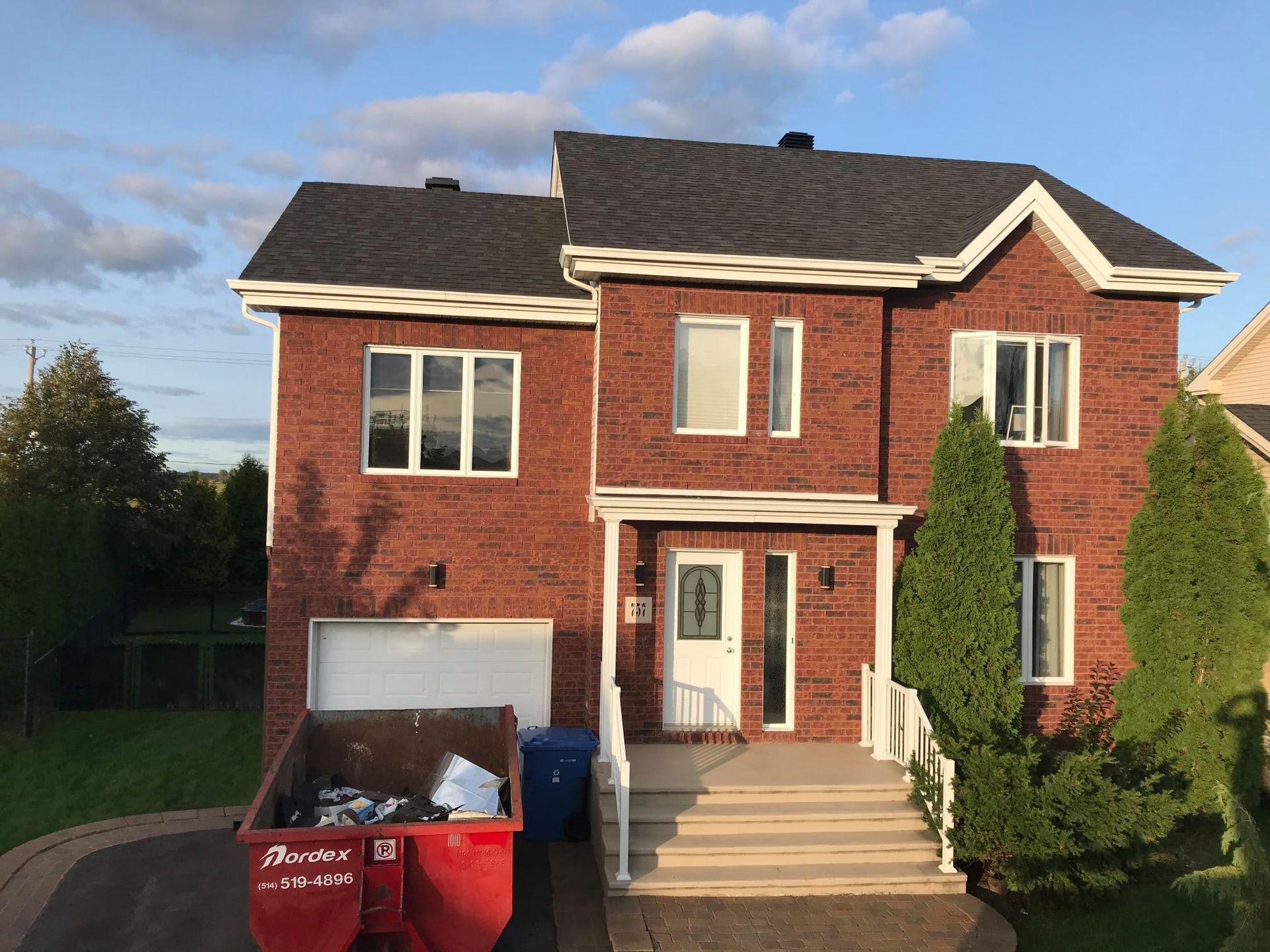 Une grande maison en briques avec une benne à ordures devant
