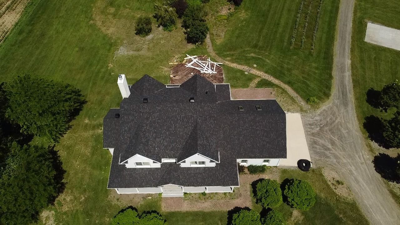 Une vue aérienne d'une grande maison au toit noir entourée d'arbres et d'herbe.