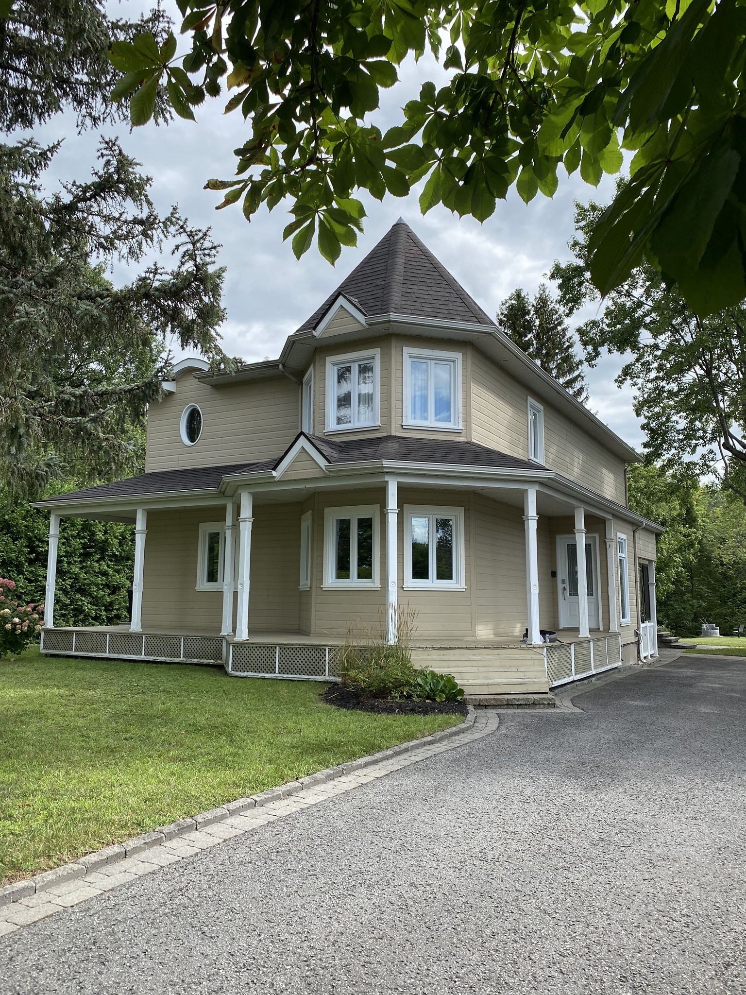 Une grande maison avec un porche et une allée est entourée d'arbres.