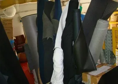 In un laboratorio disordinato, rotoli di tessuto di vari colori e consistenze sono disposti verticalmente.