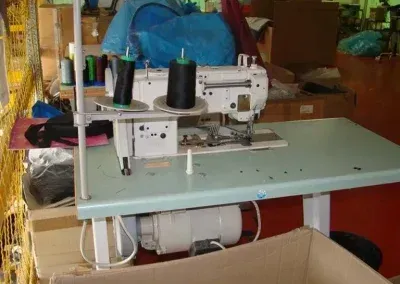 Una macchina da cucire industriale bianca con due rocchetti di filo nero, montata su un tavolo in un'officina.