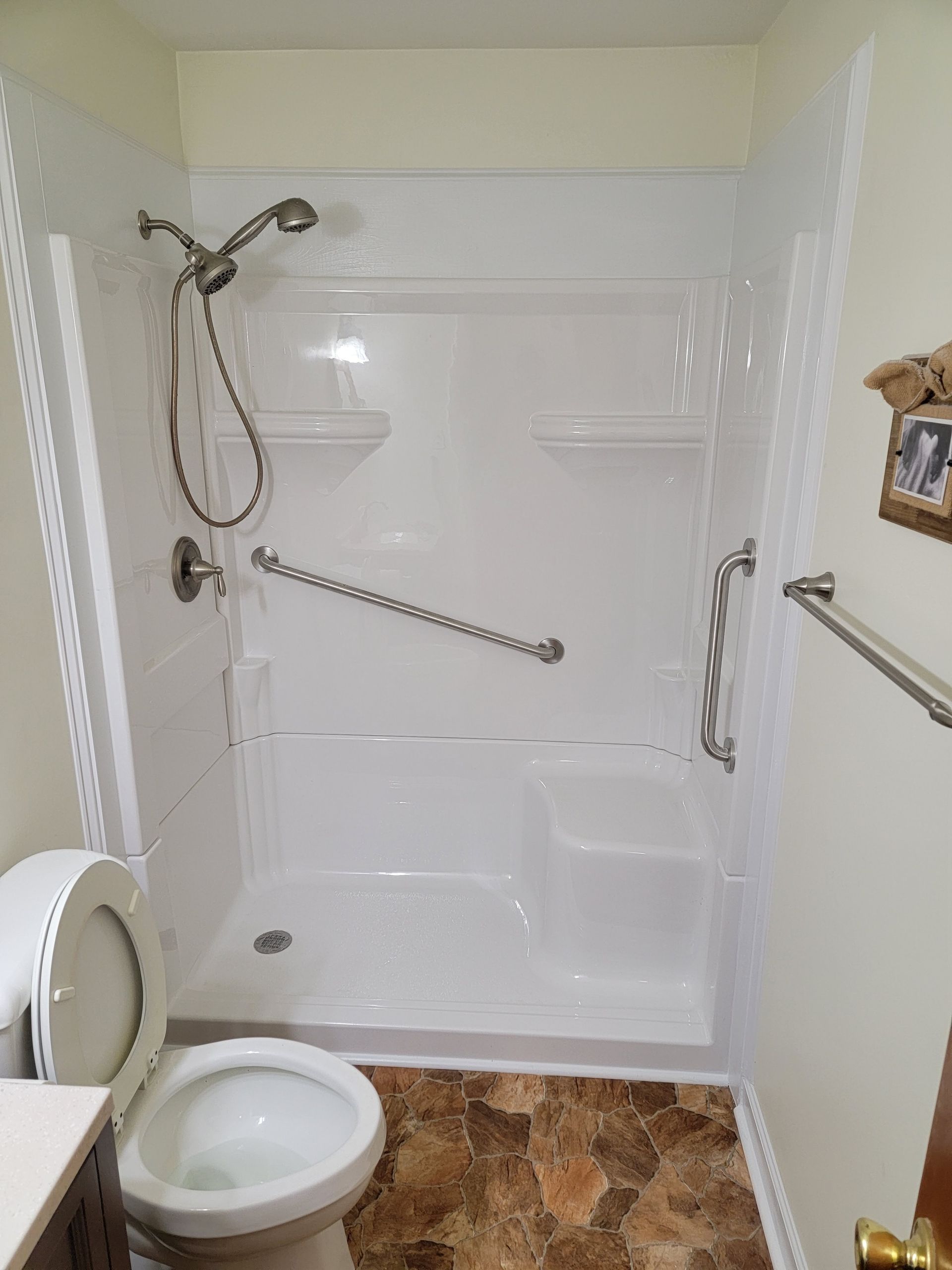 A bathroom with a toilet , shower , and handrails.