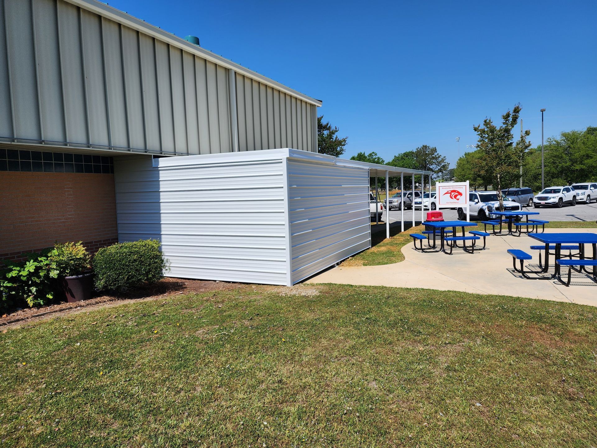 A white building with blue picnic tables in front of it.