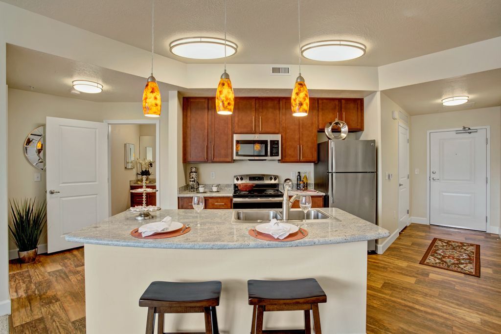 A kitchen with a large island , stools and a refrigerator.