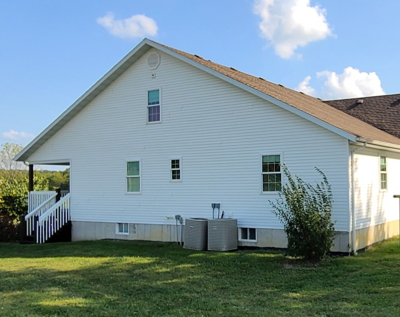 A white house with a brown roof sits in the middle of a lush green field