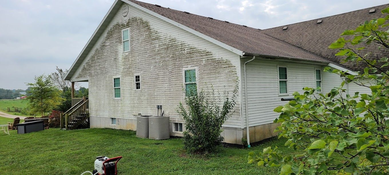 A white house with a brown roof is sitting on top of a lush green field.