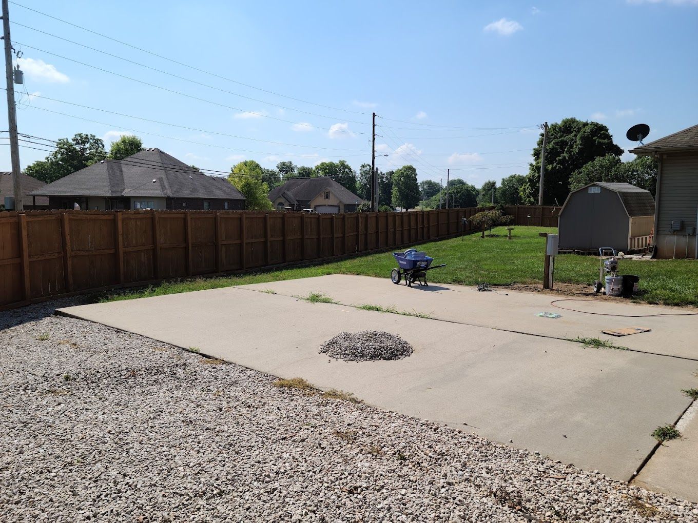 A backyard with a wooden fence and a gravel driveway