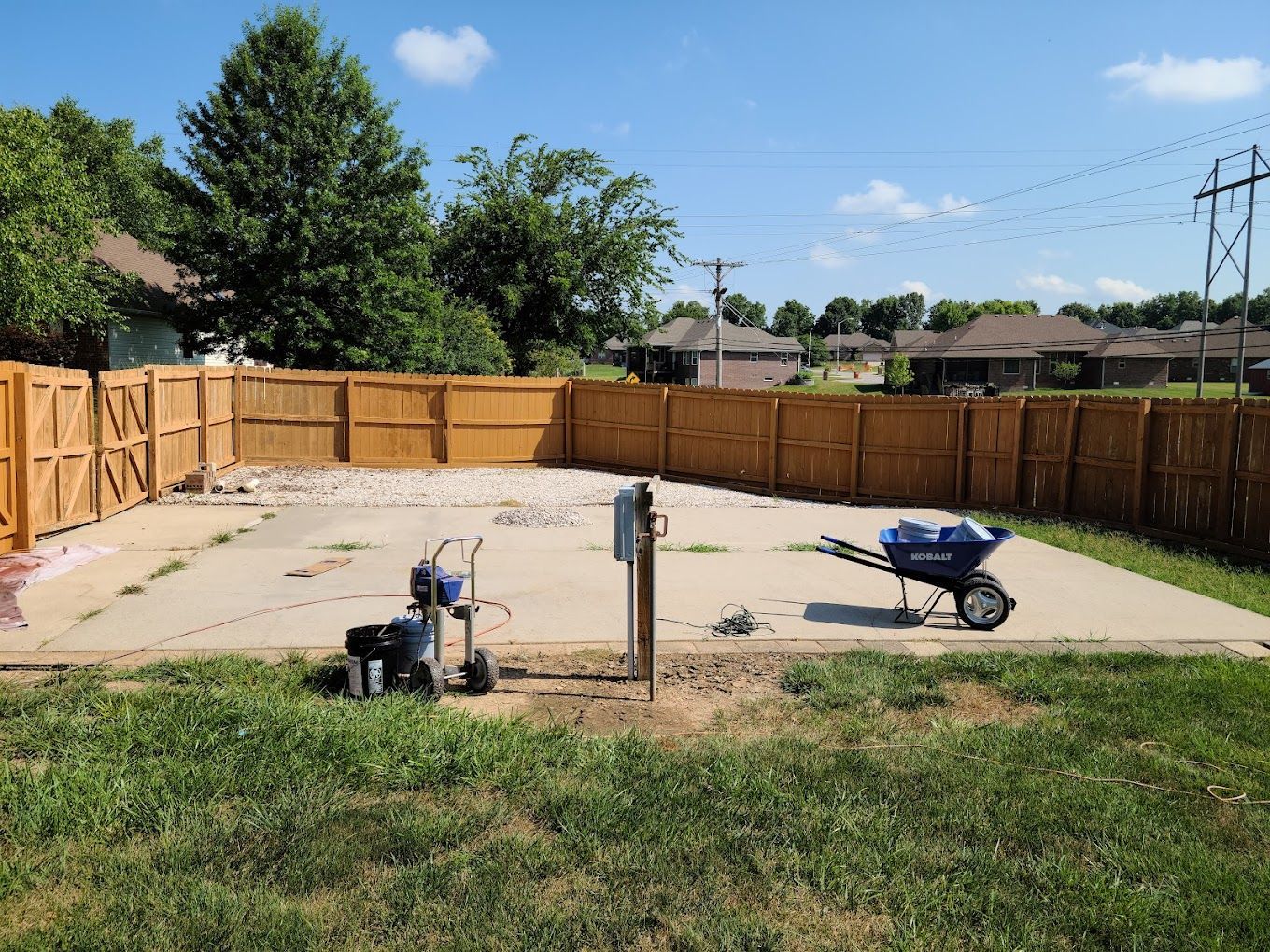 A backyard with a wooden fence and a blue wheelbarrow.