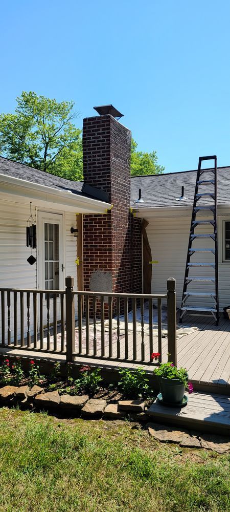 A white house with a brick chimney and a ladder in front of it.