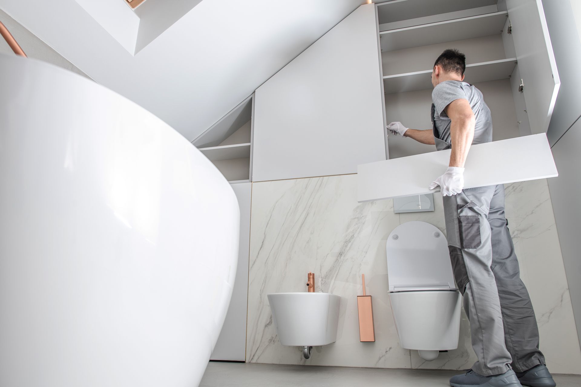 Person standing in a modern bathroom, inspecting a wall-mounted toilet and sink under a slanted ceiling