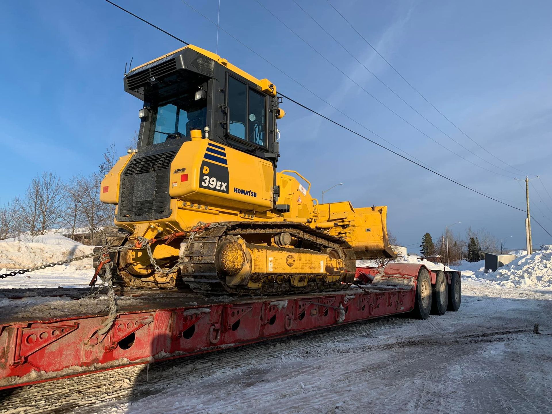 Un bulldozer jaune est assis sur une remorque rouge dans la neige.