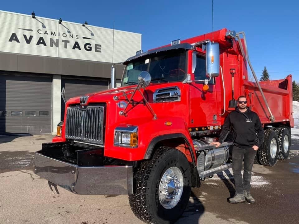 Un homme se tient devant un camion-benne rouge.