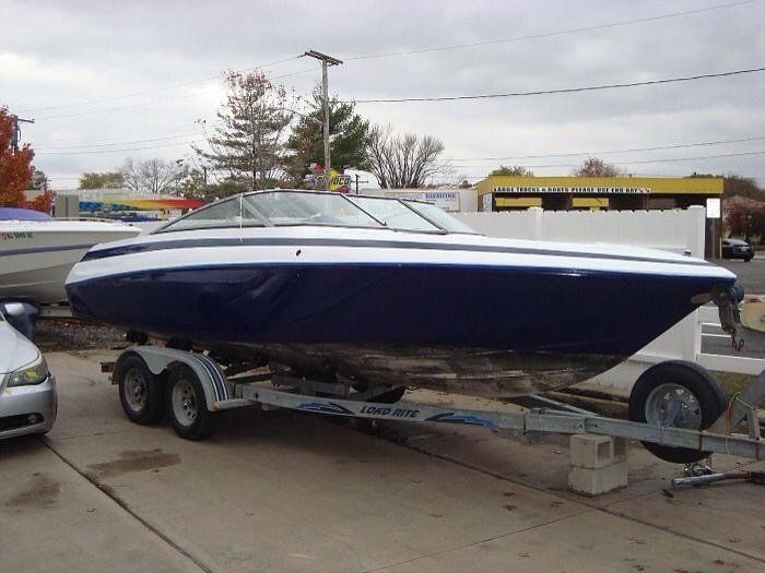 A blue and white boat is on a trailer next to a car.