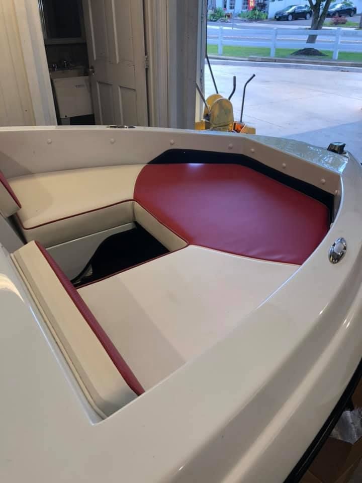 A white boat with red and white seats is sitting in a garage.