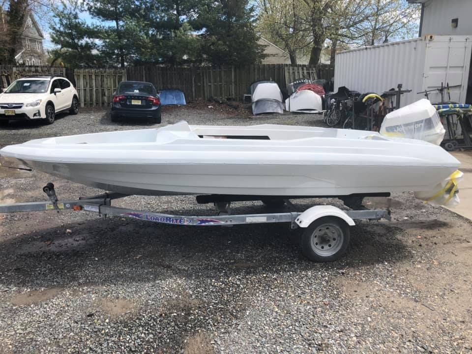 A small white boat is on a trailer in a parking lot.