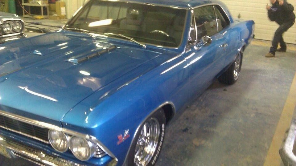 A man is standing next to a blue car in a garage.