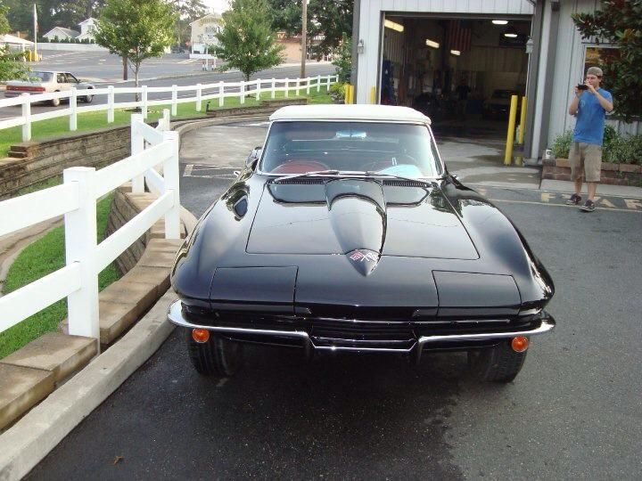 A black corvette is parked next to a white fence