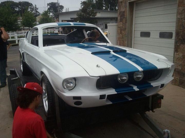 A white mustang with blue stripes is on a trailer