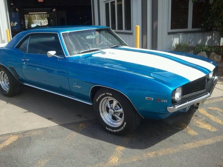 A blue car with white stripes is parked in front of a garage