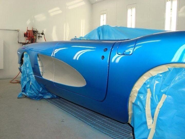 A blue car is being painted in a paint booth