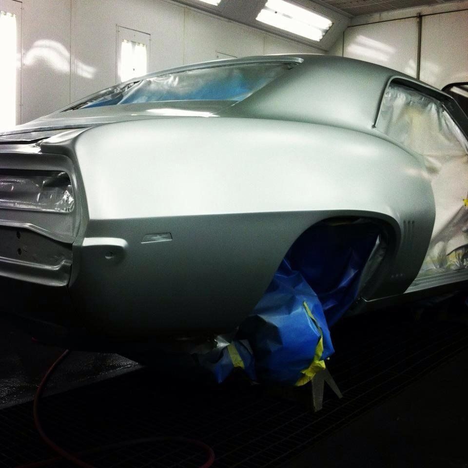 A silver car is being painted in a paint booth