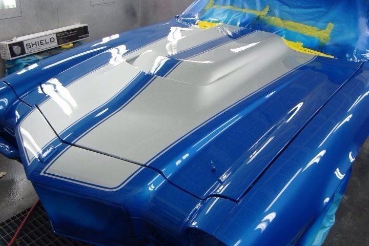 A blue car with white stripes is being painted