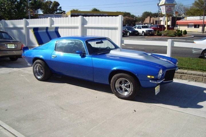 A blue car is parked in a parking lot next to a white fence