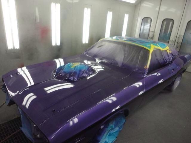 A purple car is being painted in a paint booth