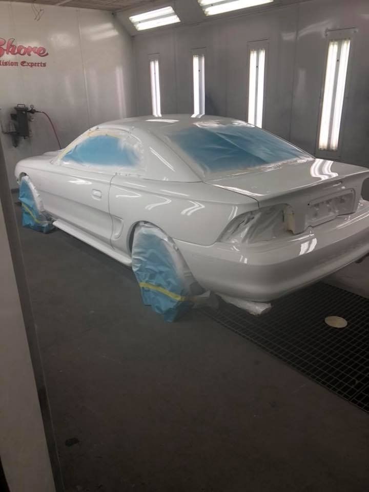 A white mustang is being painted in a paint booth.